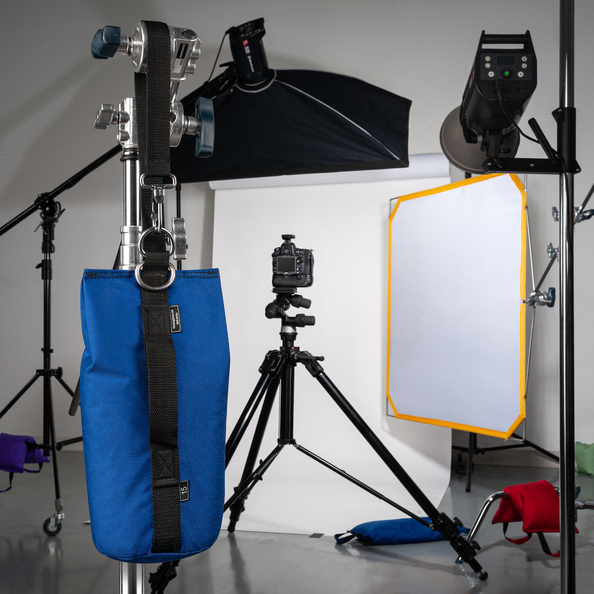 Photography studio equipment including a blue bag, camera on tripod, softbox, and light stand.