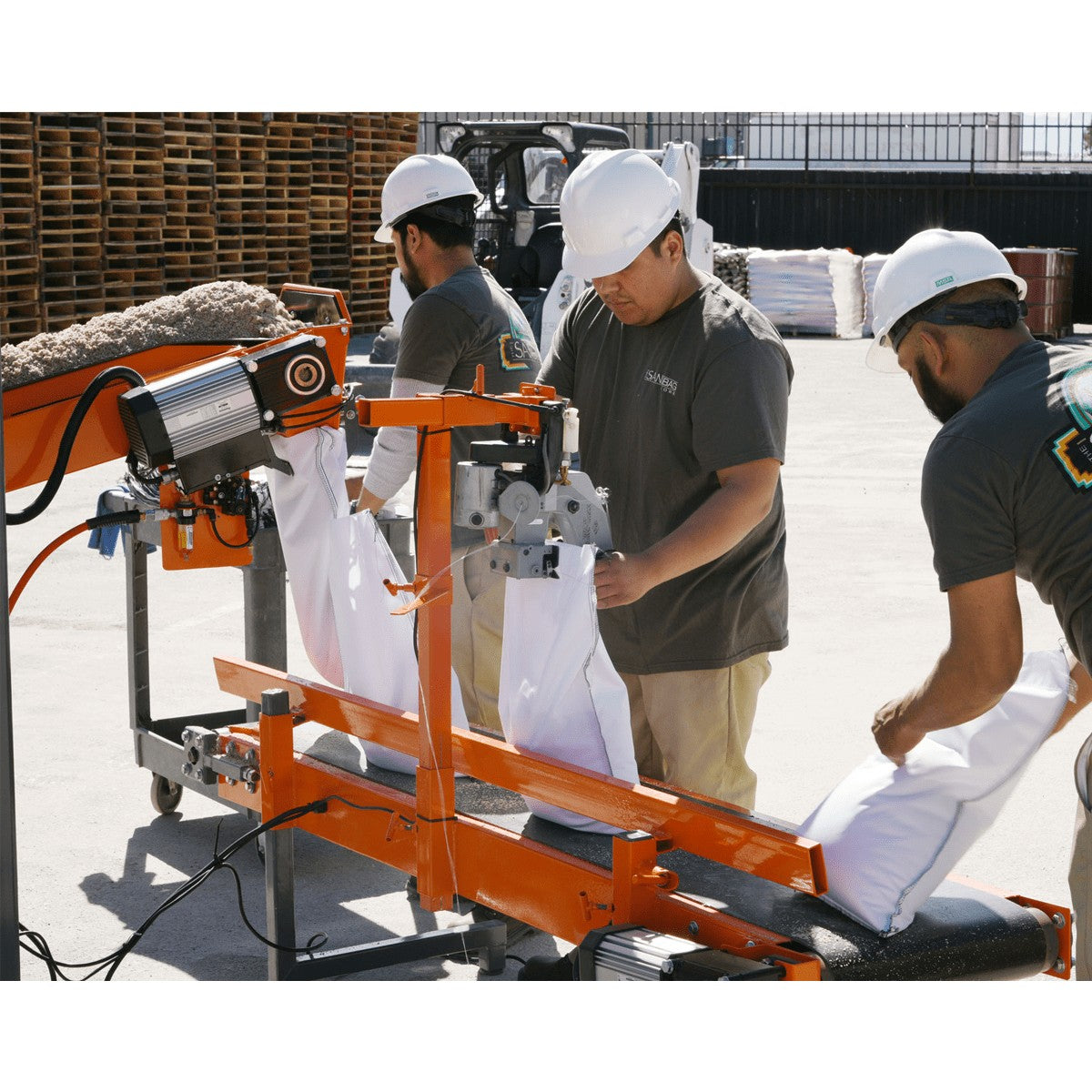 Three person crew wearing white hard hats on a bagging yard filling 1200 sandbags per hour using the Ultimate Bagger sandbag filling machine