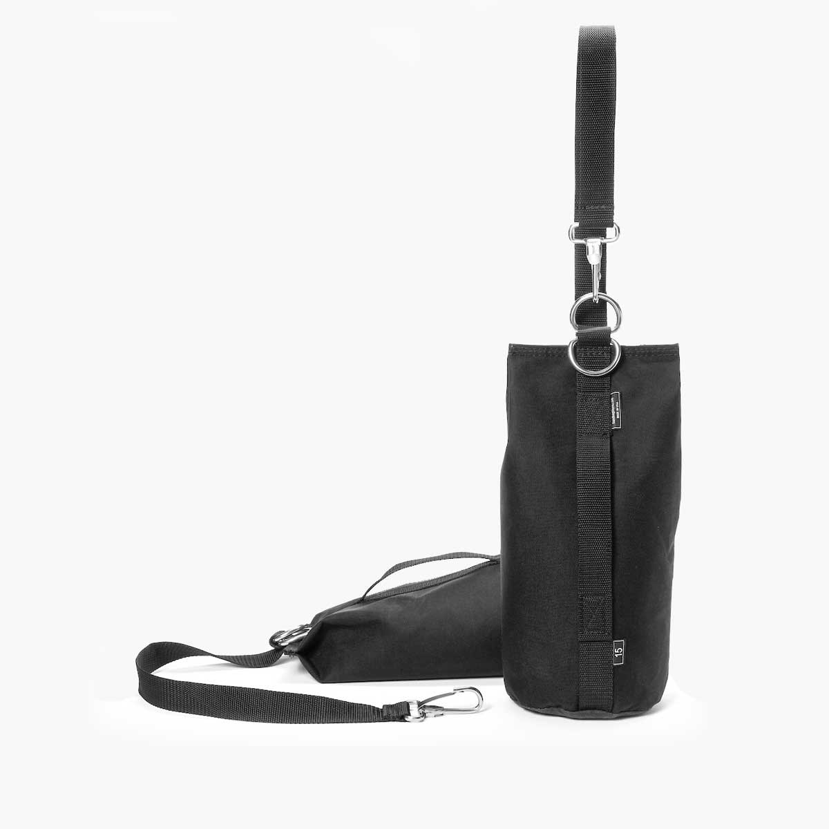 Black dropweight rigging sandbag with handle raised above bag in front of dropweight sandbag laying on back with strap detached