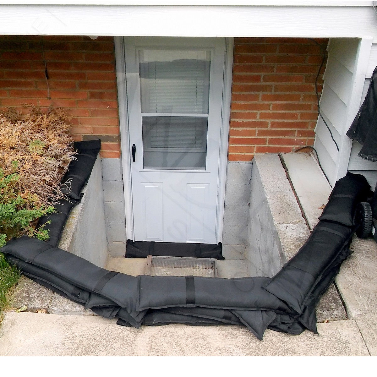Black tube sandbags surrounding a sunken basement door entrance from flooding