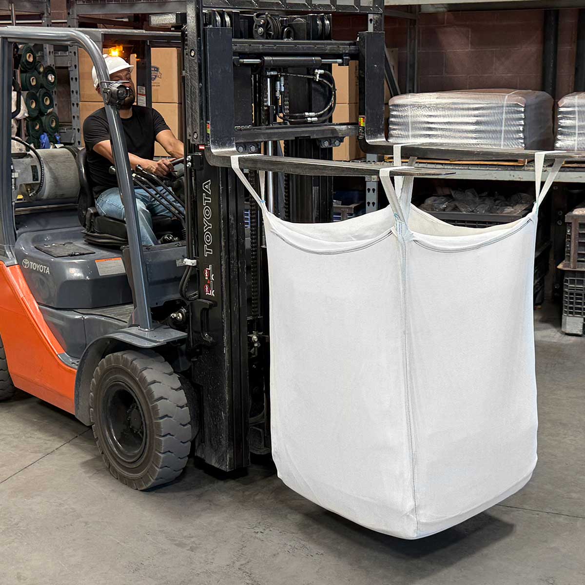 white big hoss bulk bag hoisted by forklift operated by driver in hard hat